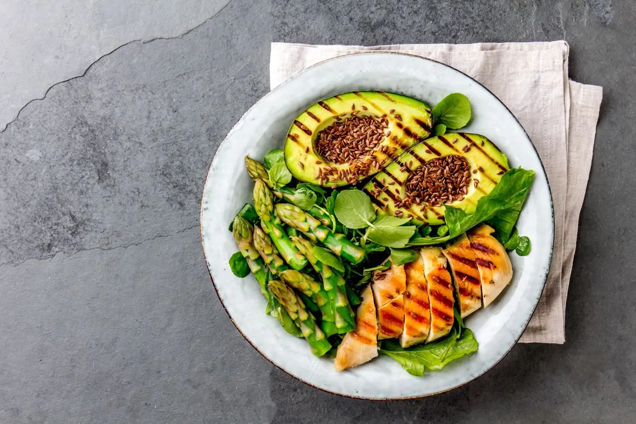 Healthy bowl with grilled chicken, avocado, asparagus, and greens.