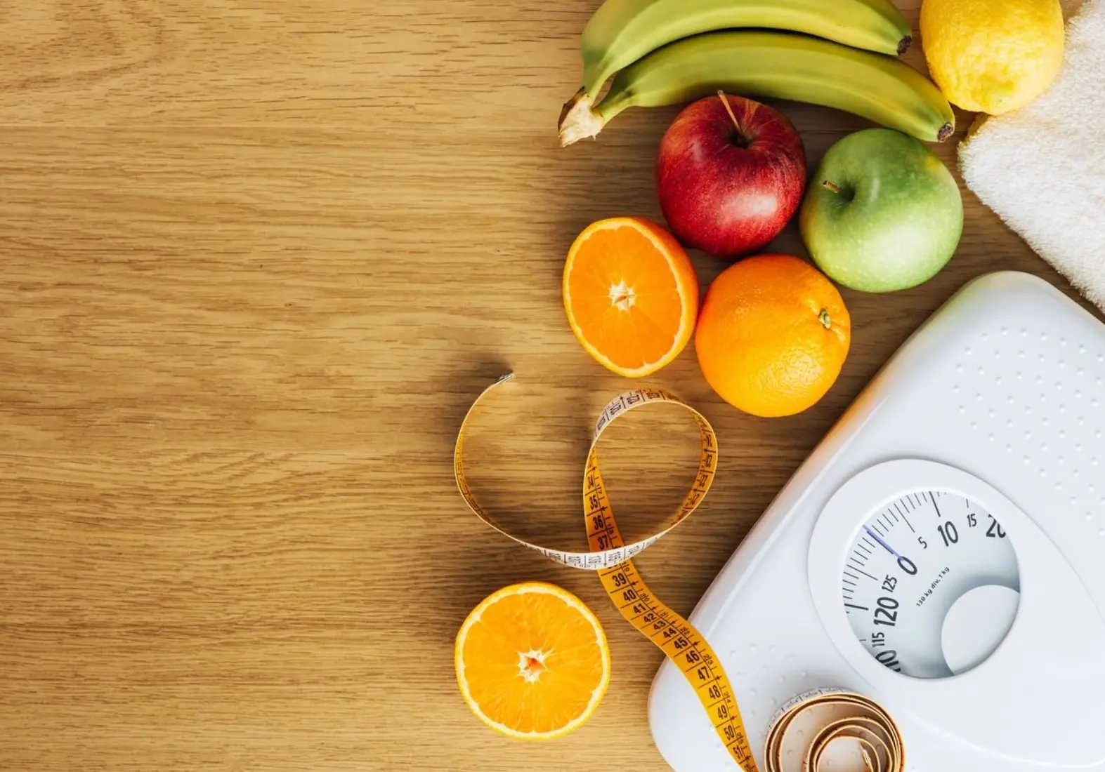Fresh fruits and a measuring tape on a wooden table with a scale.