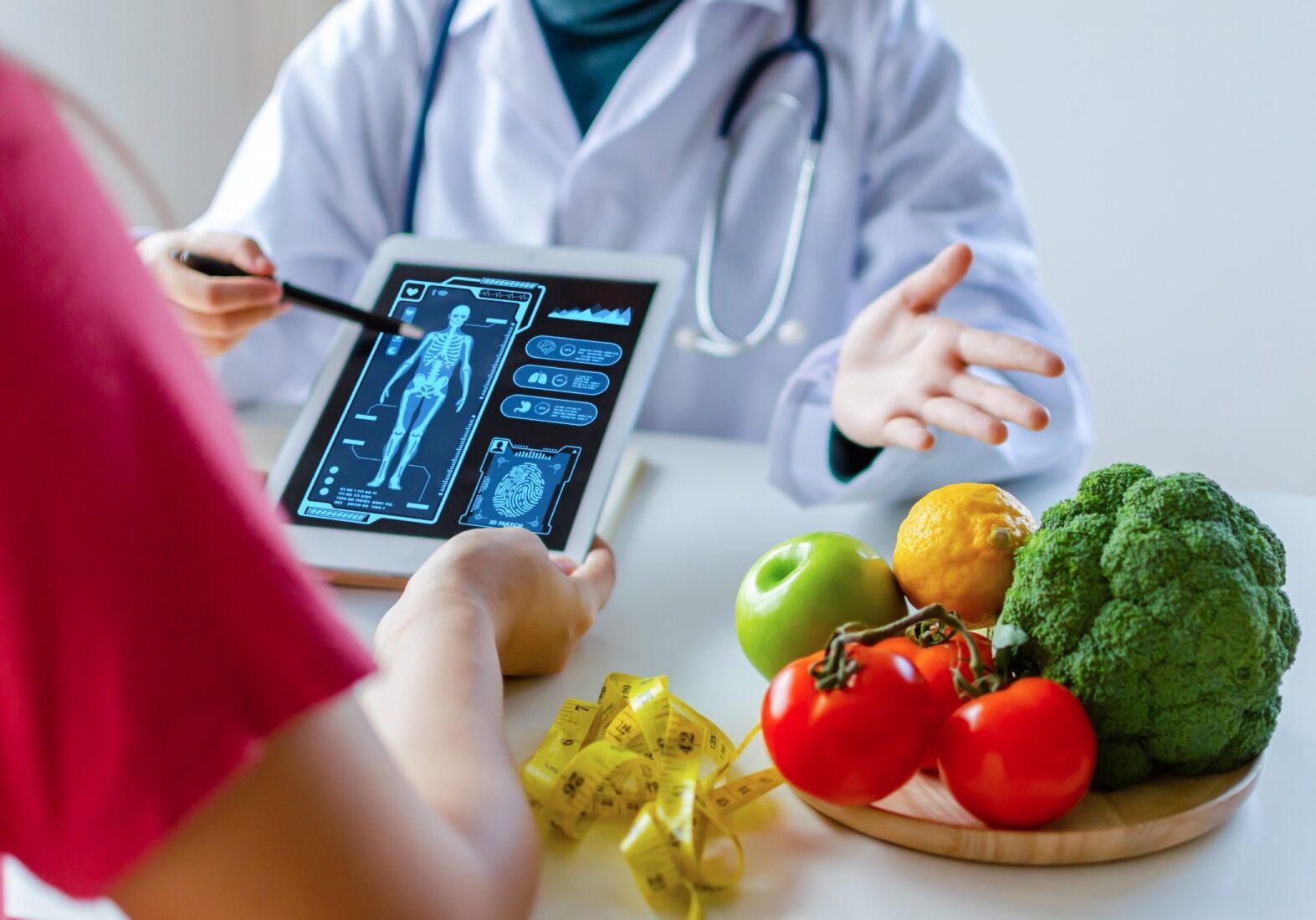 A doctor shows a digital X-ray on a tablet to a patient. Nearby, there's a plate with fruits and vegetables and a measuring tape, suggesting a discussion about health or diet.