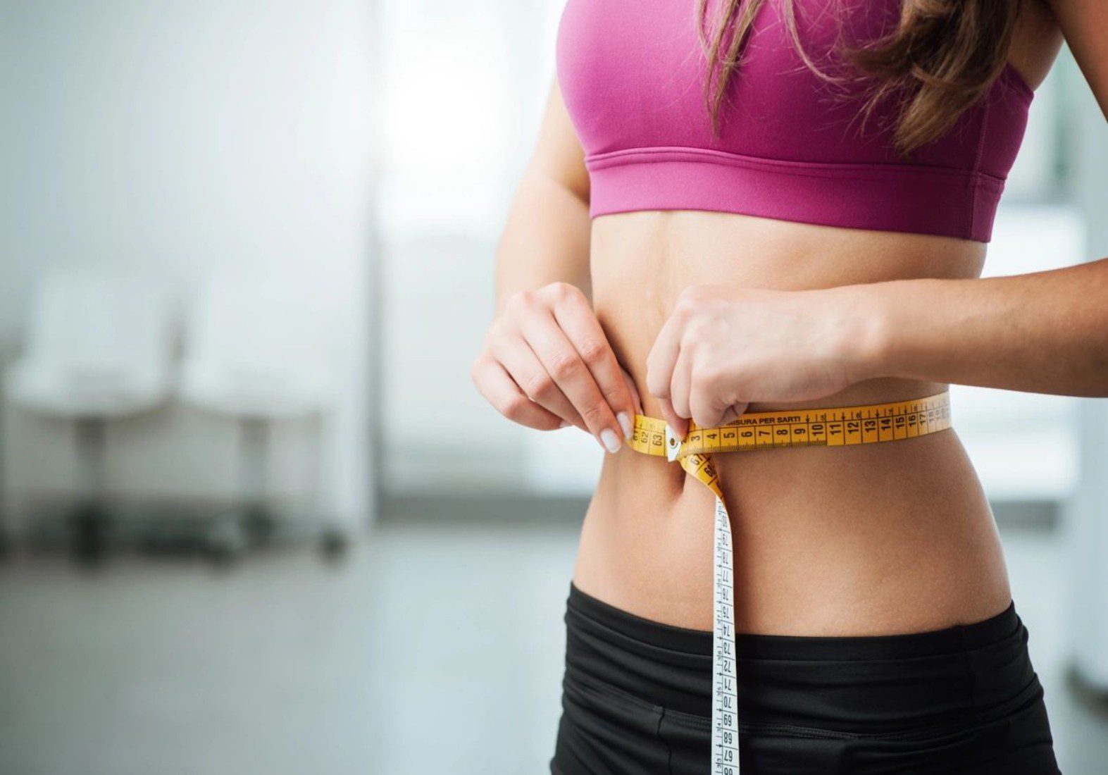 Woman measuring her waist with a tape measure during fitness check.
